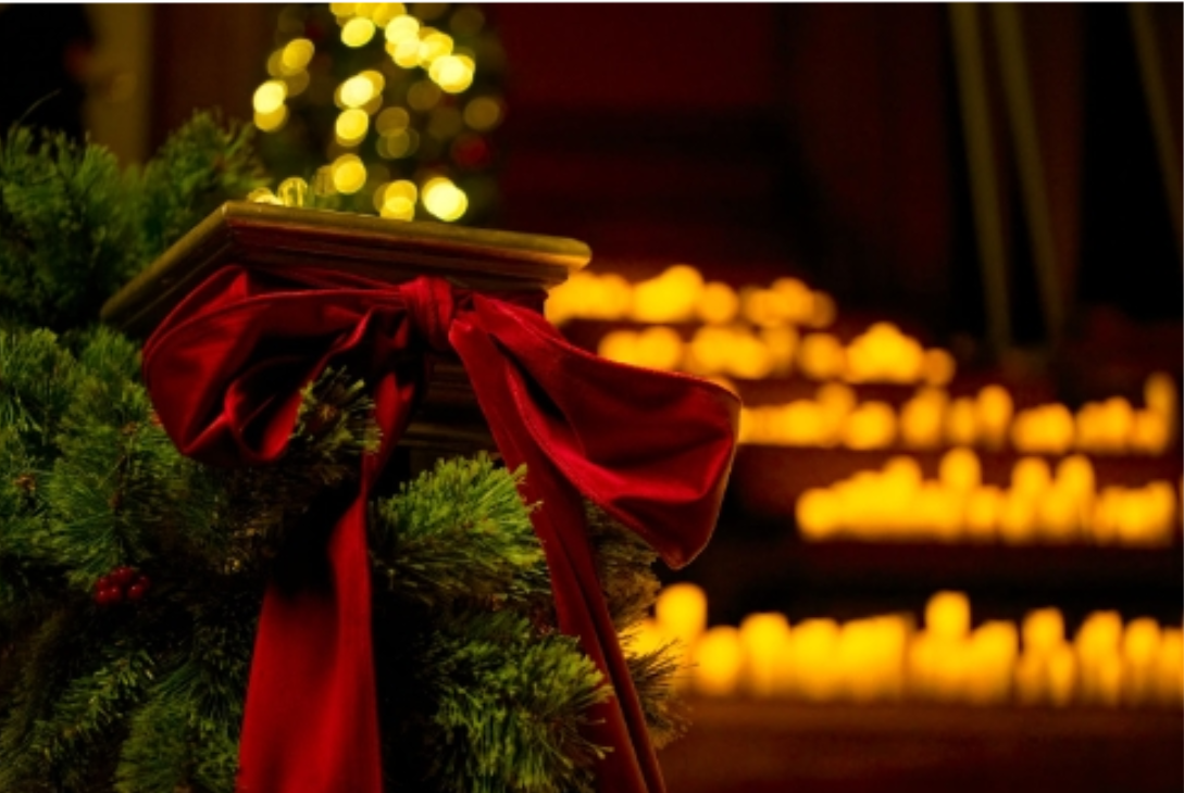 Imagem de uma árvore de natal segurando um livreto e velas ao fundo.