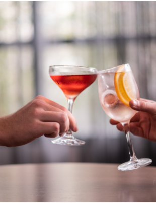 Foto de duas mãos segurando drinks alcóolicas.