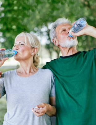Foto de dois idosos bebendo água em um parque.