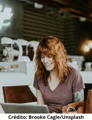 Foto ilustrativa de uma mulher ruiva utilizando o computador para possívelmente estudar.