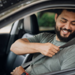 Foto ilustrativa de um homem dentro do carro colocando cinto de segurança.