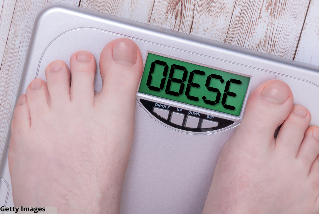 Imagem ilusttrativa de uma pessoa se pesando numa balança com o resultado em inglês sinalizando obeso.