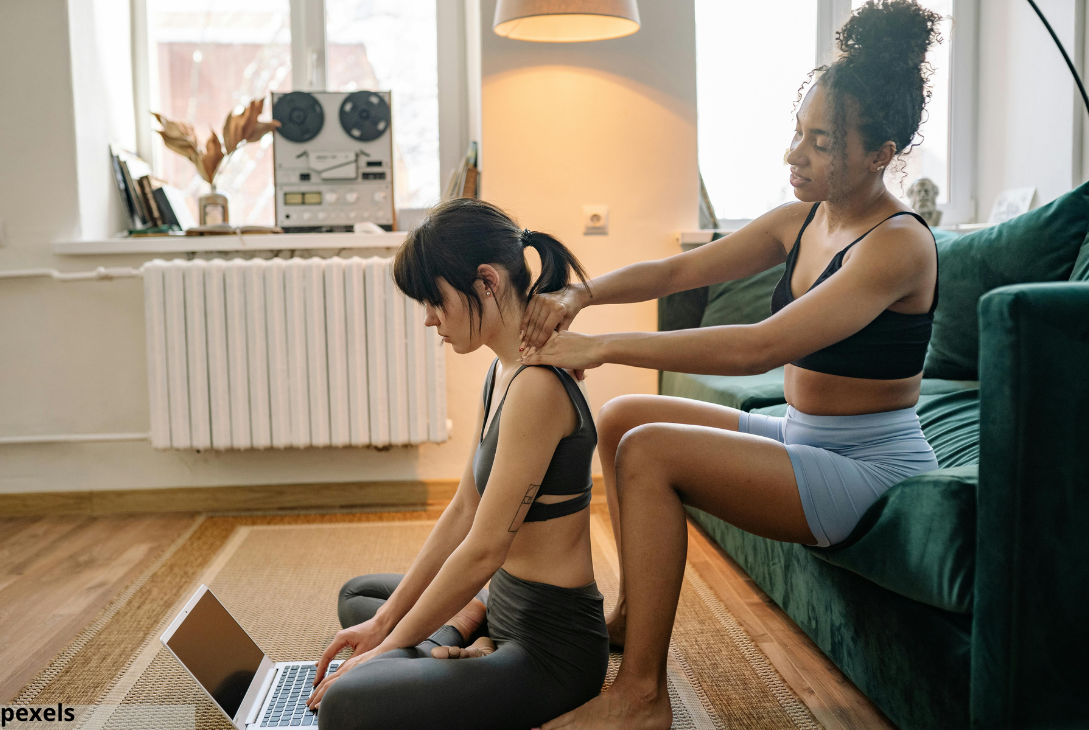 Foto ilustrativa de uma mulher massageando os ombros de uma outra mulher.