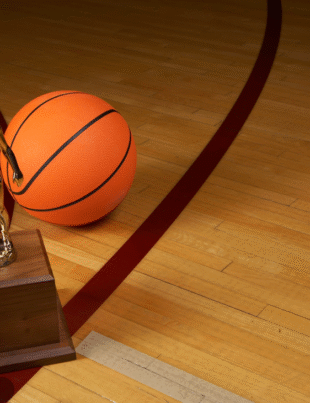 Foto ilustrativa de uma quadra de basquete com uma bola de basquete e um troféu.
