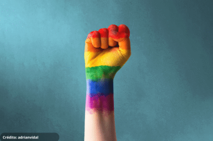 Foto de um punho cerrado com as cores pintadas da bandeira LGBTQIA+.