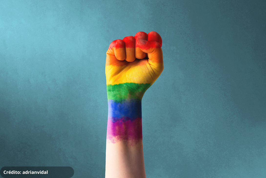Foto de um punho cerrado com as cores pintadas da bandeira LGBTQIA+.