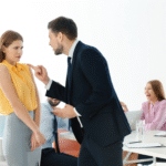 A imagem ilustrativa mostra uma mulher sendo intimidada por seu colega de trabalho enquanto outros funcionários dão risadas ao fundo.