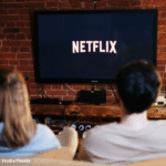 Imagem ilustrativa de um casal olhando para a TV com logotipo da Netflix.