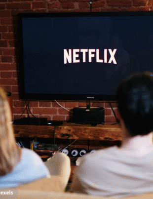 Imagem ilustrativa de um casal olhando para a TV com logotipo da Netflix.