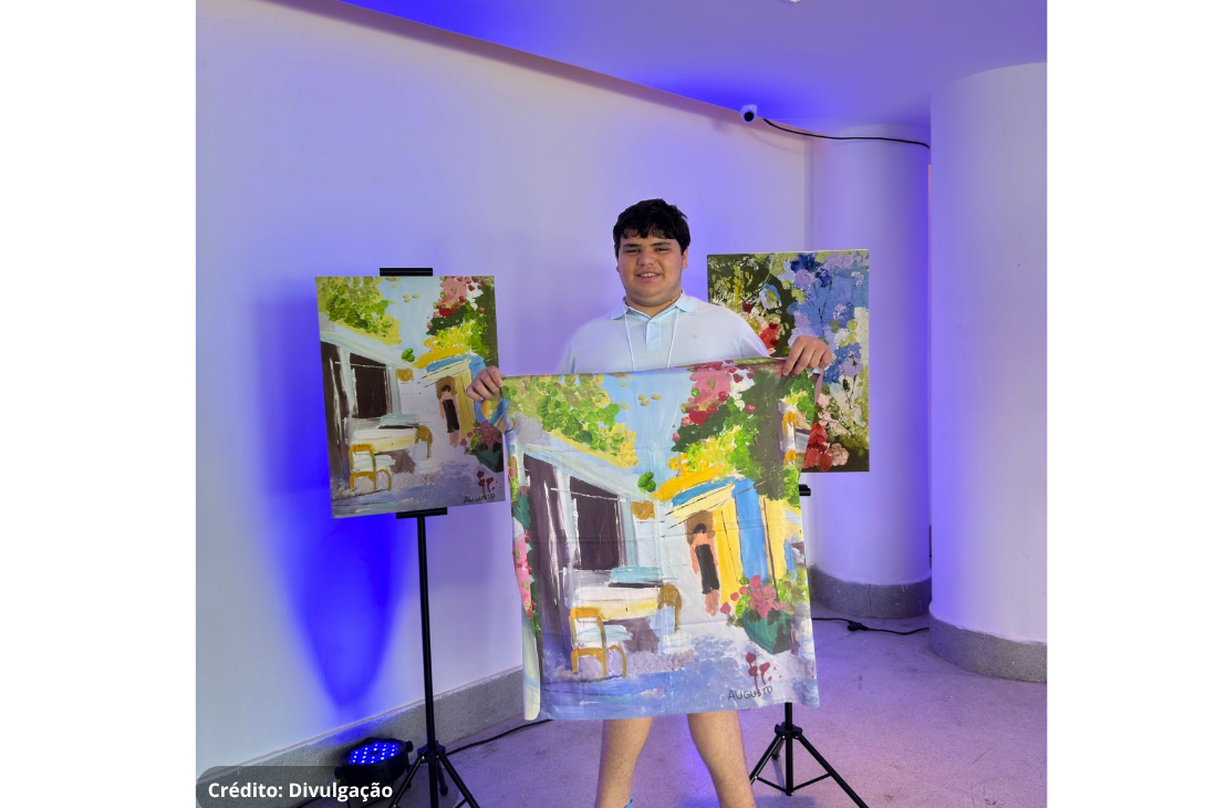 Foto do artista que mostra orgulhoso alguns de seus quadros que viraram estampas de lenços.