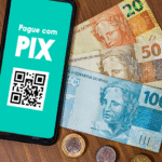 Imagem ilustrativa de uma mesa com dinheiro em notas e moedas e um celular com Pix na tela.