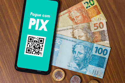 Imagem ilustrativa de uma mesa com dinheiro em notas e moedas e um celular com Pix na tela.