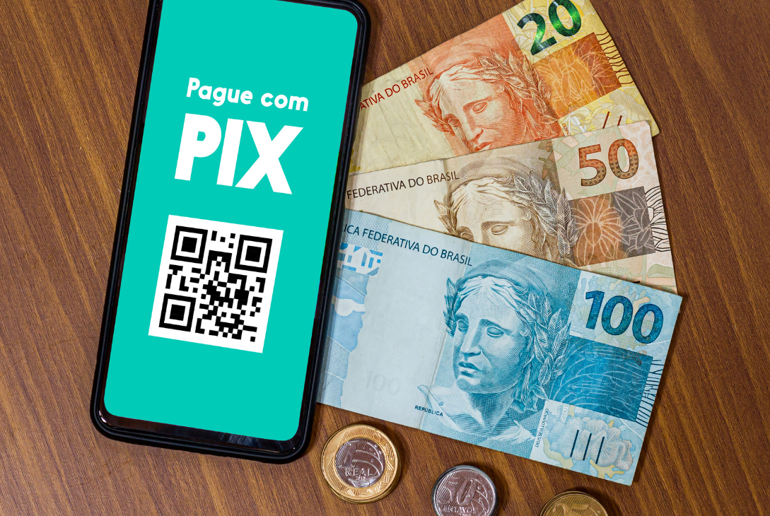 Imagem ilustrativa de uma mesa com dinheiro em notas e moedas e um celular com Pix na tela.